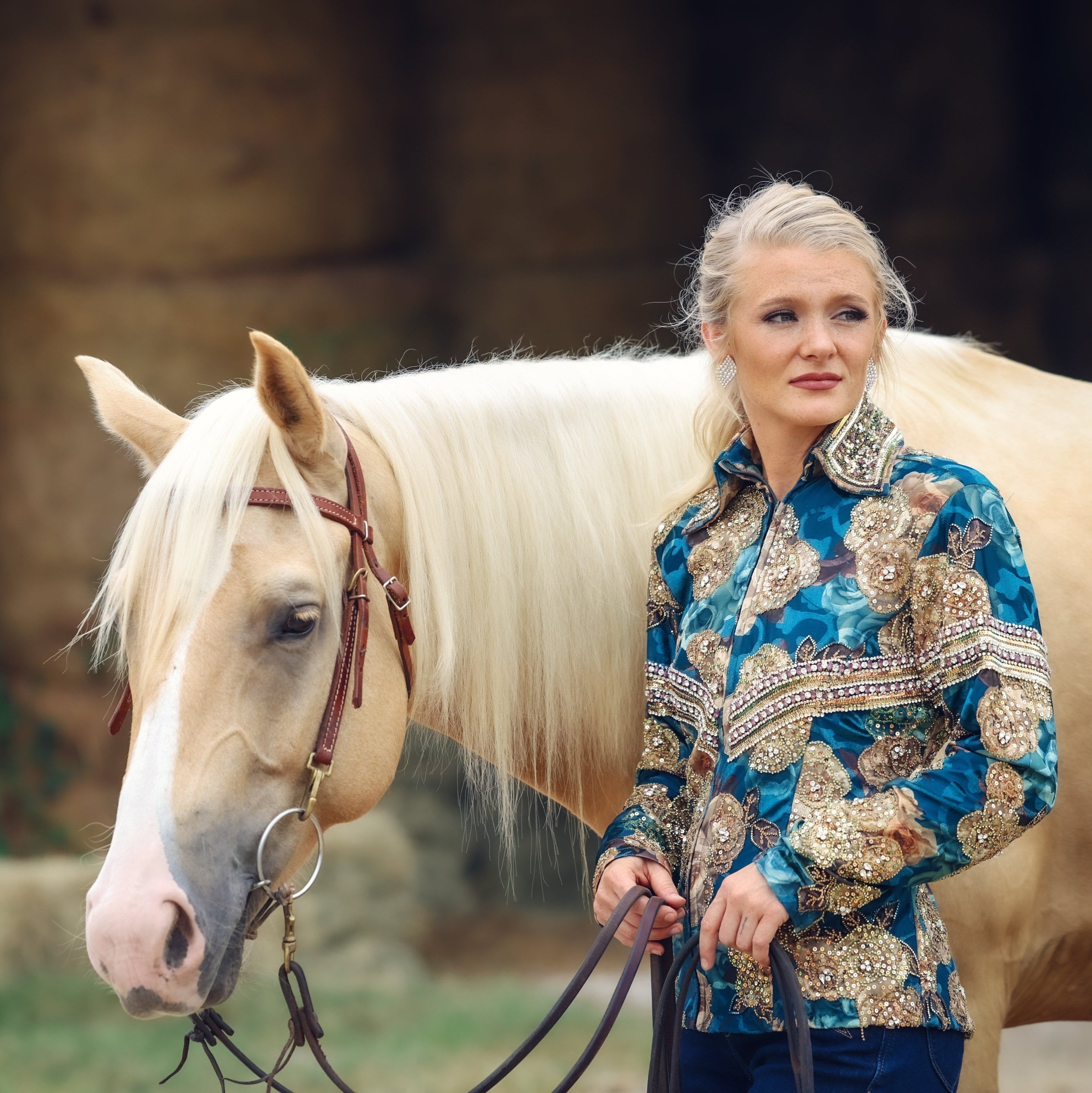 Woman in colorful riding jacket and cowboy hat standing next to a horse on a road