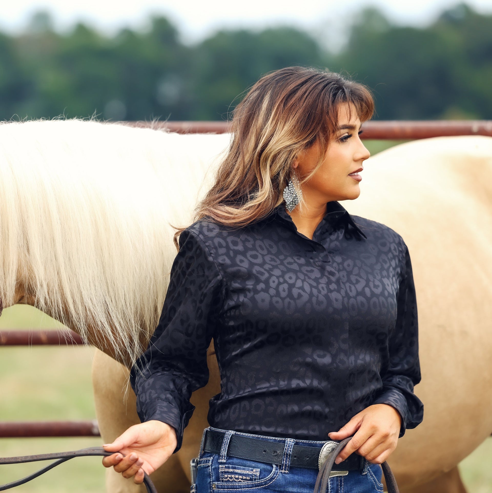 Model with horse posing in leopard black shirt from the Faith collection by Kultured Rider in a green field.