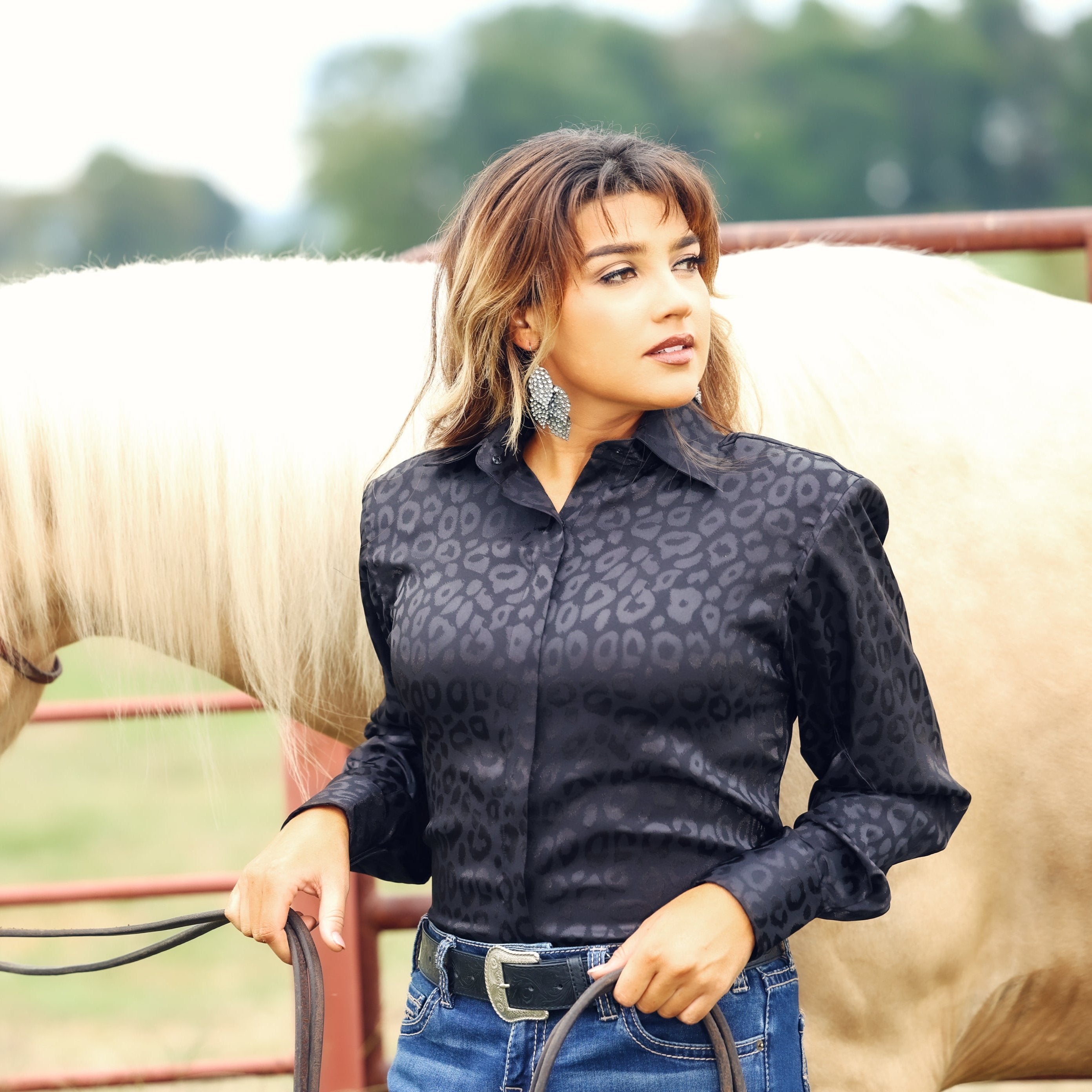 Model with horse posing in leopard black shirt from the Faith collection by Kultured Rider in a green field.