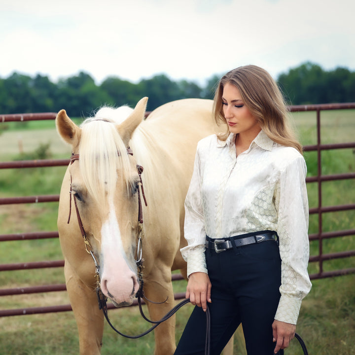 Model with horse posing in white lace shirt from the Faith collection by Kultured Rider in a green field.