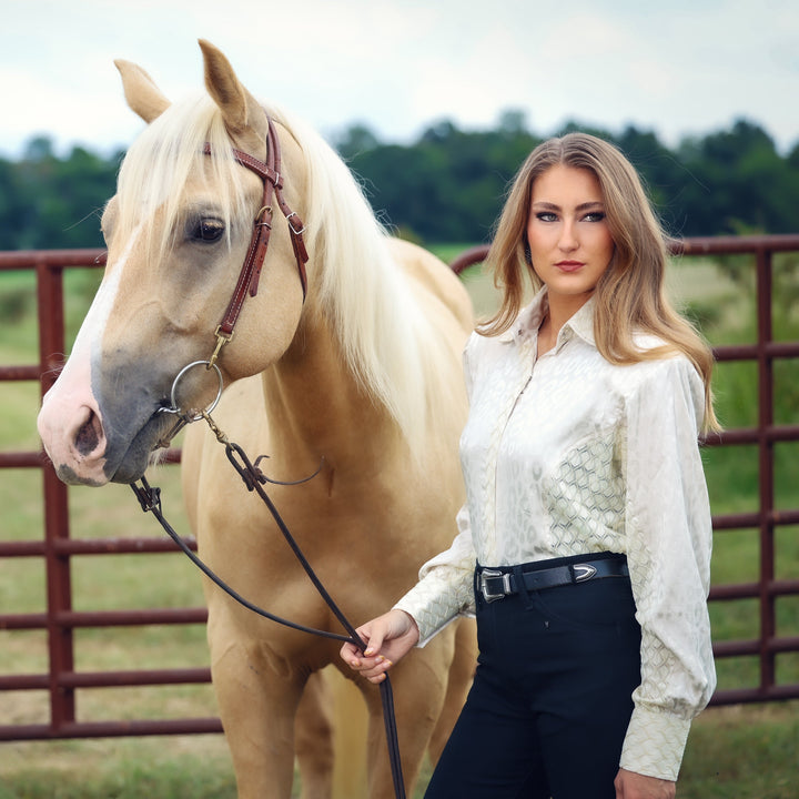 Model with horse posing in white lace shirt from the Faith collection by Kultured Rider in a green field.