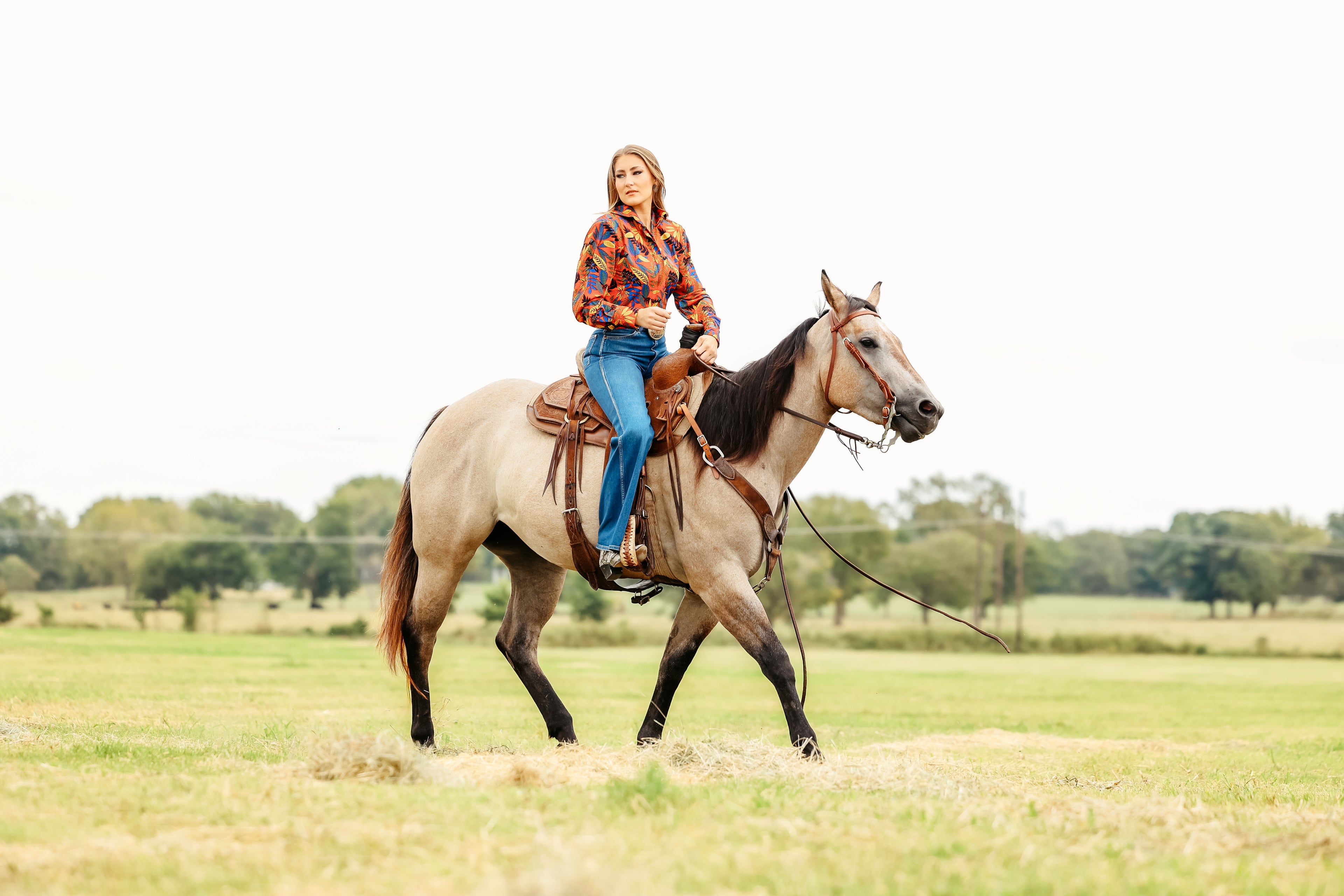 Model on horse posing in jungle red shirt from the Romina collection by Kultured Rider in a green field.