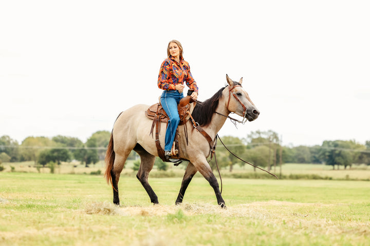 Model on horse posing in jungle red shirt from the Romina collection by Kultured Rider in a green field.