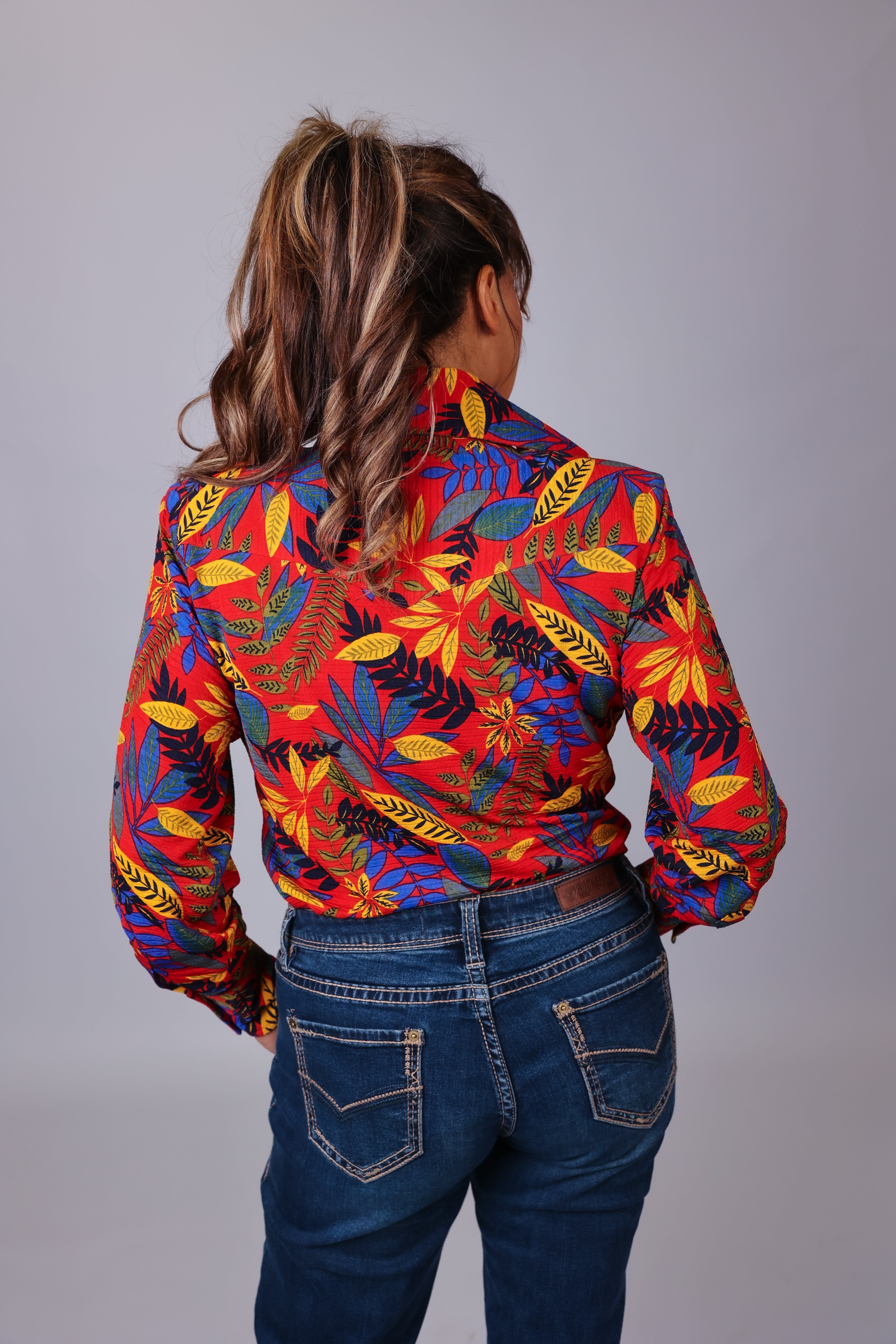 Model posing in jungle red shirt from the Romina collection by Kultured Rider in front of a studio backdrop.